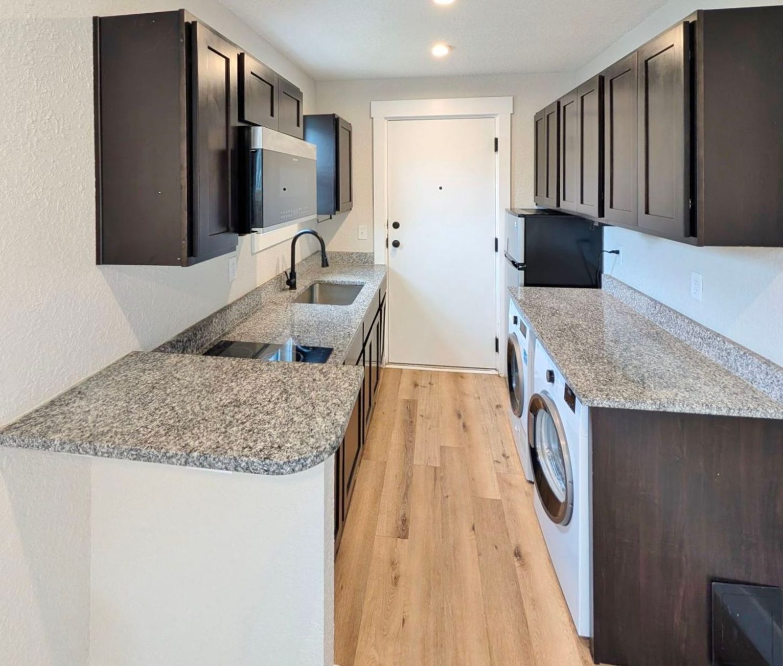 Galley kitchen with granite countertops, dark cabinets, and a washer and dryer at Ashley Lofts